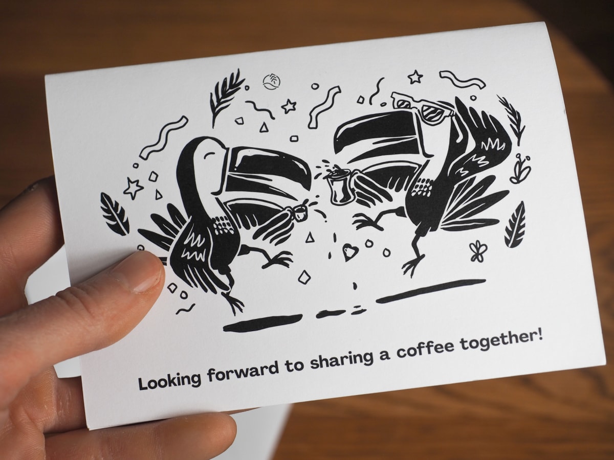 Photo of a hand holding a new postcard, showcasing the Pink Bourbon coffee from Marco Fidel Rodriguez